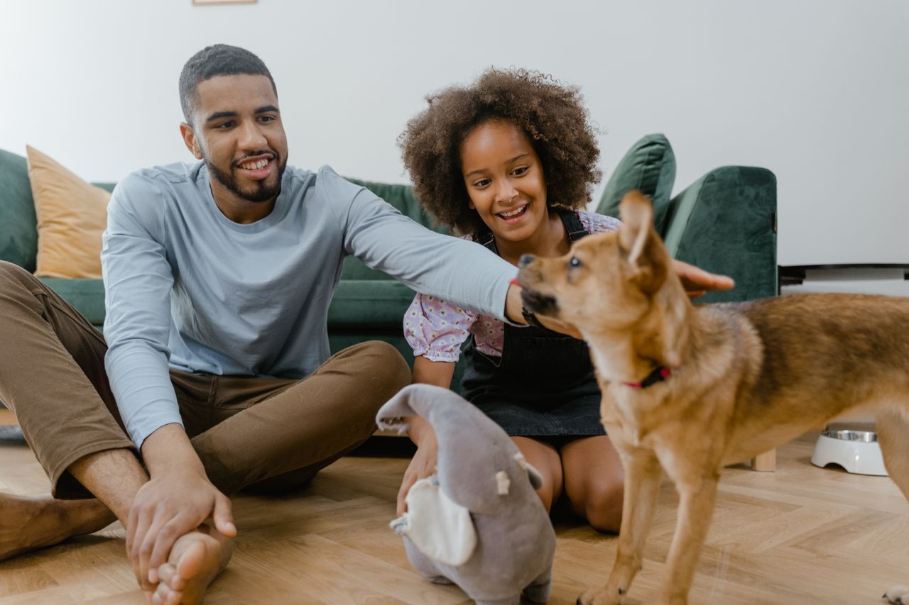 Man and girl enjoying quality time with their dog indoors, promoting family bonding.